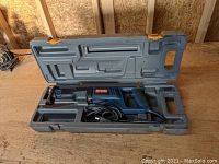 Full view of the Ryobi reciprocating saw inside the gray molded hard carrying case with orange latches, laying open on a wooden surface.