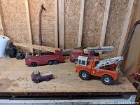 Four vintage Tonka steel toys and one vintage scooter displayed on a wooden surface in a workshop environment.