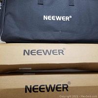 Black nylon carrying case with Neewer logo atop two cardboard stand boxes
