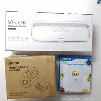 Boxes and packaging of VPCOK Vacuum Sealer, Aicok Hand Mixer HM833, and Renpho Smart Nutrition Scale ESSNG01W showing model names and brands