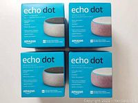 Four Amazon Echo Dot 3rd Generation smart speakers in original blue packaging, two grey and two pink boxes.