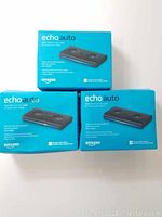 Three boxed Amazon Echo Auto devices stacked in blue packaging showing product name and image.