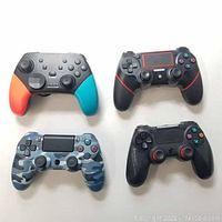 Four wireless gaming controllers displayed flat, showing button layouts and colors.