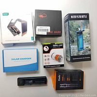 Overview of all boxed camping items including solar charger, fishing reel, mosquito lamp, water filter bottle, TDS EC meter, and flashlight