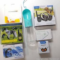All items on white background including branded boxes for dog muzzle, no bark collar, ultrasonic device, collapsible bowls, rechargeable collar, and pet bottle.
