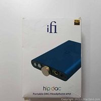Front view of original white retail box with iFi branding, Hi-Res Audio logo, image of blue Hip DAC with volume knob and headphone ports visible. Retail box indicates product is a portable DAC/headphone amp.