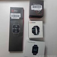 Three smart watch boxes: tall black box for Orit CS201, white L8star, and black/red smartwatch box; displayed on white surface.