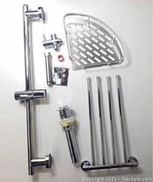 Photo of assembled metal bathroom pieces including corner shelf, towel racks, metal rods, drain stopper and small hardware parts on white background.
