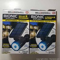 Front view of two boxed Bell+Howell Bionic Solar Powered spotlights showing product branding and features including no batteries or wires needed, 8 super bright LED lights, solar powered, motion detection up to 25 feet, weather resistant, swivel action, and environmental friendliness.