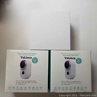 Two boxed Yulinca wireless security cameras showing front packaging with camera image and feature icons.