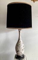 Full view of the lamp showing the black fabric shade with beige trim and tall marble-look ceramic base.
