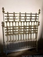 Full view of the headboard showing white iron frame and brass decorative rings and finials