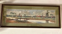 Long rectangular framed watercolor landscape with windmill, water, trees, and figure crossing a wooden plank bridge, signed bottom left corner.