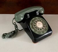 Side angle of the vintage rotary dial telephone showing the black base and green handset with coiled cord.