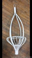 Vintage white painted rattan plant holder with rounded basket and looped hanger on wood floor background