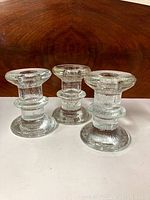 Three vintage clear textured glass candle holders arranged side by side on a white surface with a wood grain background.