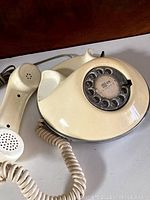 Image showing the whole cream-colored rotary phone with handset placed beside it, on a wooden surface.