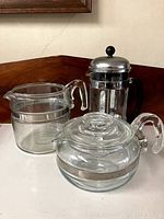 Photo showing three glass teapots including a Pyrex teapot and a French press style coffee maker.