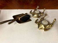 Two brass turkey-shaped tea light holders and a brass crumb tray with a matching broom sweeper arranged on a white surface.
