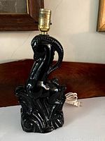 Overall front view of black glazed ceramic antelope lamp with brass socket and white cord