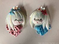 Pair of vintage ceramic dog head wall pockets on light surface, one with pink and one with blue polka-dot ribbons.