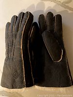 Top view of a pair of black sheepskin gloves laid flat on a surface, showing the outside leather and stitching detail.