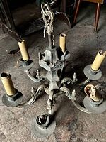 Full view of antique metal ceiling light fixture on floor showing five candle-style bulb holders with worn sleeves and decorative base.