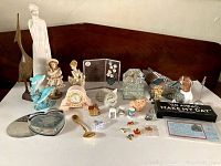 Photo showing multiple figurines including tall ceramic figurine, blue dolphin glass figurines, small pink clock, and others