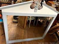 Front view of large rectangular wood framed mirror with white paint and triangular pediment top with finial.