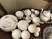 Photo of tea set components on table showing plates, saucers, cups, teapot, creamer, sugar bowl, salt and pepper shakers arranged neatly.