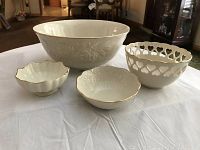 Four assorted Lenox bowls displayed on a white tablecloth. One large embossed bowl, one pierced bowl with hearts, and two small scalloped edge bowls with gold rims.
