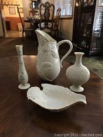 Four Lenox porcelain pieces displayed on a wooden table including the pitcher, vases, and shell-shaped dish.