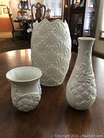 Three white porcelain Lenox vases displayed on a wooden table, showing size and pattern differences.