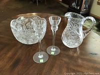 Photo shows the crystal bowl, pitcher, and two candlesticks placed on a wooden table, illustrating the overall set.