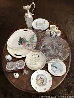 Overview of all items on a wooden table including plates, glass clear plates, pitcher, small measuring cups, bell figurines, candle holders.
