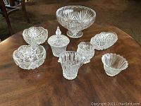Set of 8 assorted crystal items displayed on wooden table, showing details of patterns and shapes.