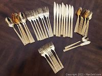 Full set of gold-tone cutlery laid out showing knives, forks, tablespoons, teaspoons, salad forks, spreader, and sugar spoon.