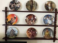 Photo of all nine decorative collector's plates arranged on a wooden display shelf, showing detailed artistic scenes with no visible damage.