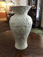 Front view of 16 inch tall white Lenox vase with detailed embossed floral design and flared rim.