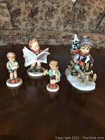 Four Goebel Hummel figurines displayed together showing front details and scale against couch background.