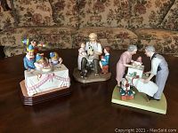 Three assorted Norman Rockwell porcelain figurines shown from above on a wooden table in front of a floral couch.