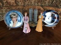 Lot of assorted collectors pieces on table including decorative plates, figurines, and model.