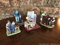 Five Norman Rockwell inspired figurines arranged on a table with floral couch background