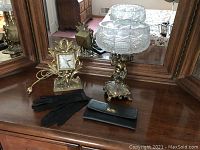 Photo showing the full lot on a wooden surface with mirror background including the clock, crystal bowl on cherub base, black gloves, and wallet.
