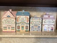 Full set of 4 ceramic village canister jars for sugar, flour, tea, coffee. Display front view showing detailed paint and condition.