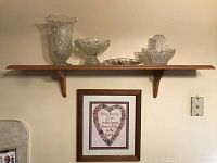 Full view of the wooden wall shelf with four crystal items arranged on top and a framed print hung below.