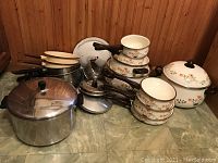 Overview of assorted pots and pans including enamel Countryside Collection items with floral decoration and stainless steel Faberware items with wooden handles.