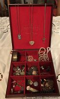 Full view of red Bentley's jewelry box showing various necklaces hanging inside along with rings, bracelets, and other small jewelry pieces in the compartments below.