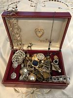 Top view of assorted jewelry pieces placed inside a red Rolex branded jewelry box with cream interior.