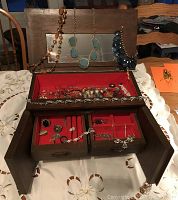 Jewelry box open showing hanging necklaces and interior compartments with assorted rings, bracelets, and earrings.